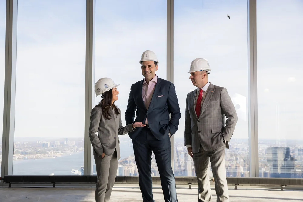 Commercial real estate executives in hard hats reviewing a project overlooking the New York skyline
