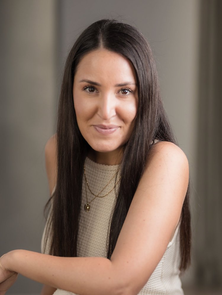 Natural headshot of a woman with long dark hair in a cream knit top on a grey background