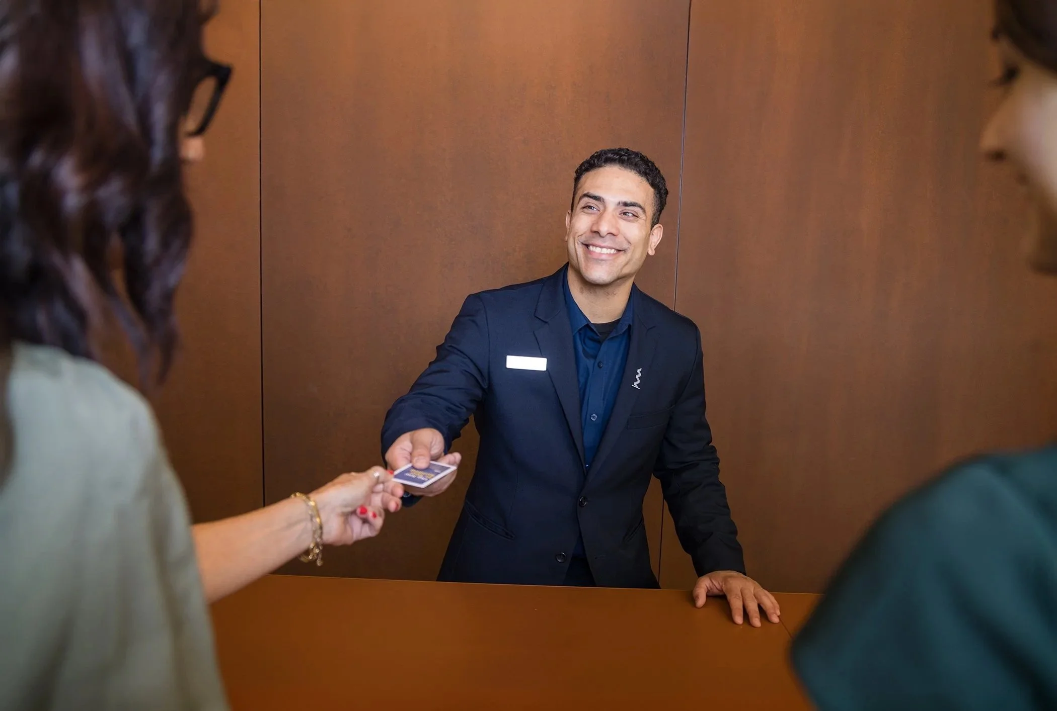 Front desk clerk handing a key card to a guest at a hotel reception counter, smiling.