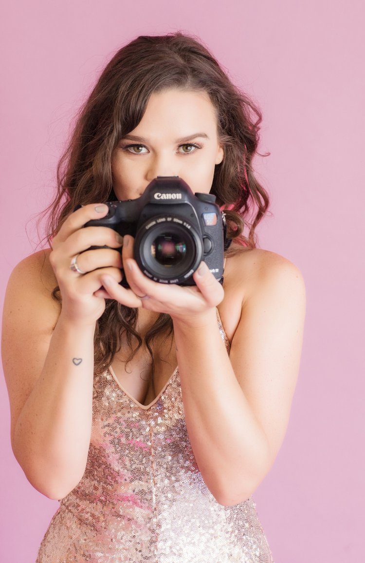 Personal branding portrait of a photographer holding a camera on a pink background