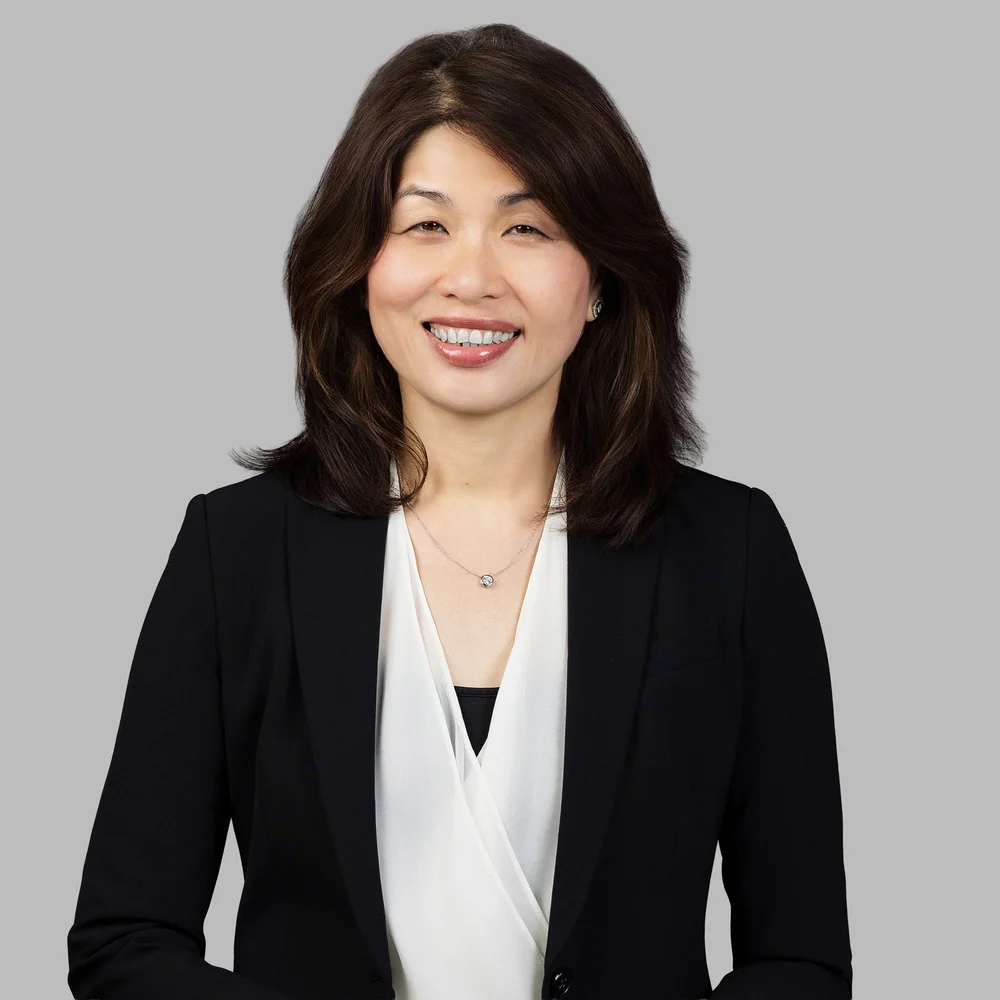Tenant headshot of a woman in a black blazer and white blouse on a grey background