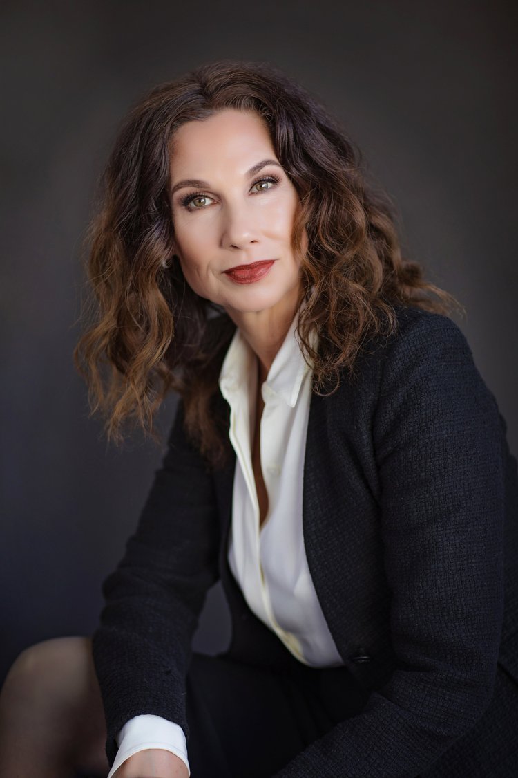 Studio headshot of an attorney with wavy hair in a black blazer on a dark background