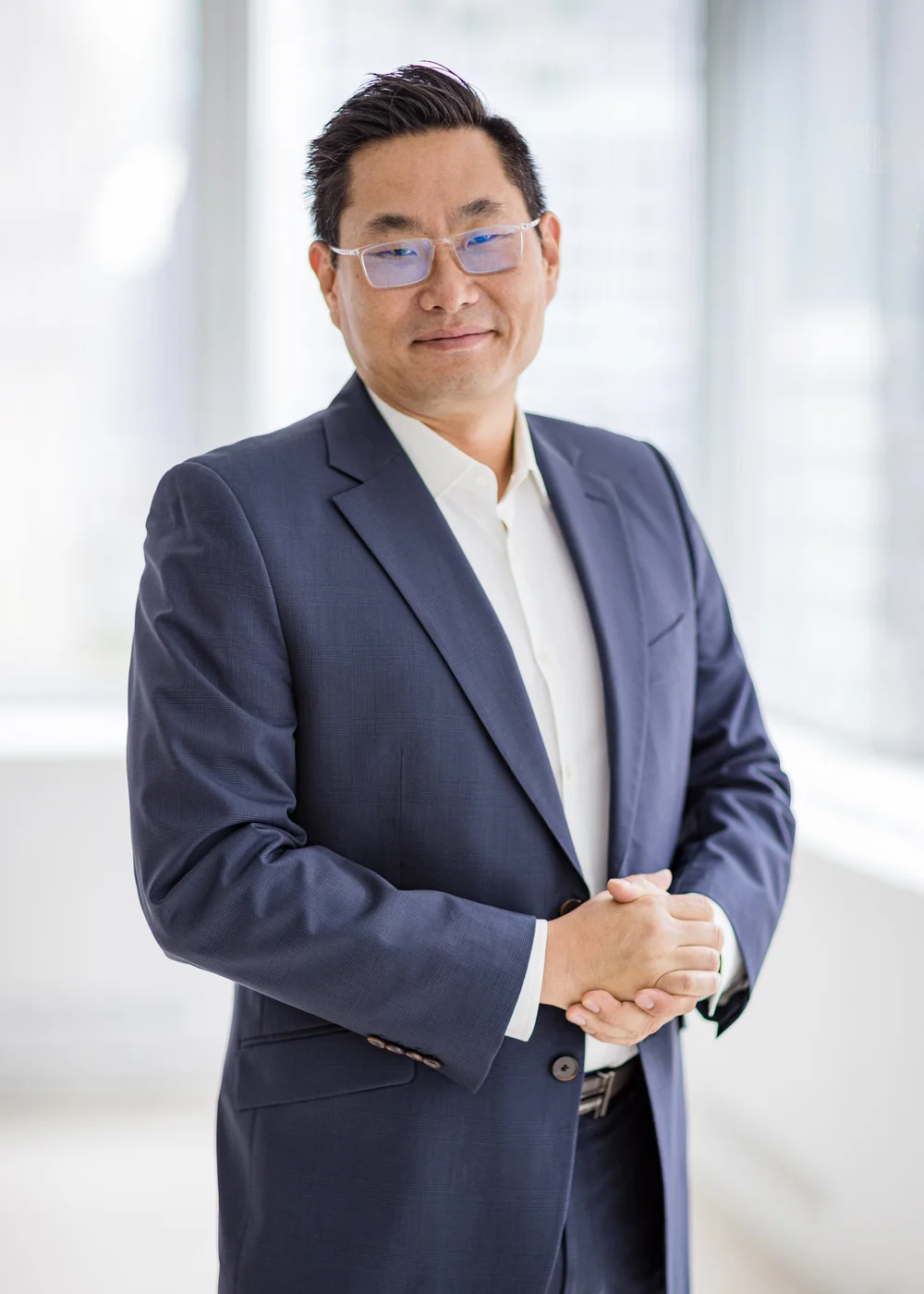 CEO headshot of a man in glasses and a navy suit in a bright, airy office