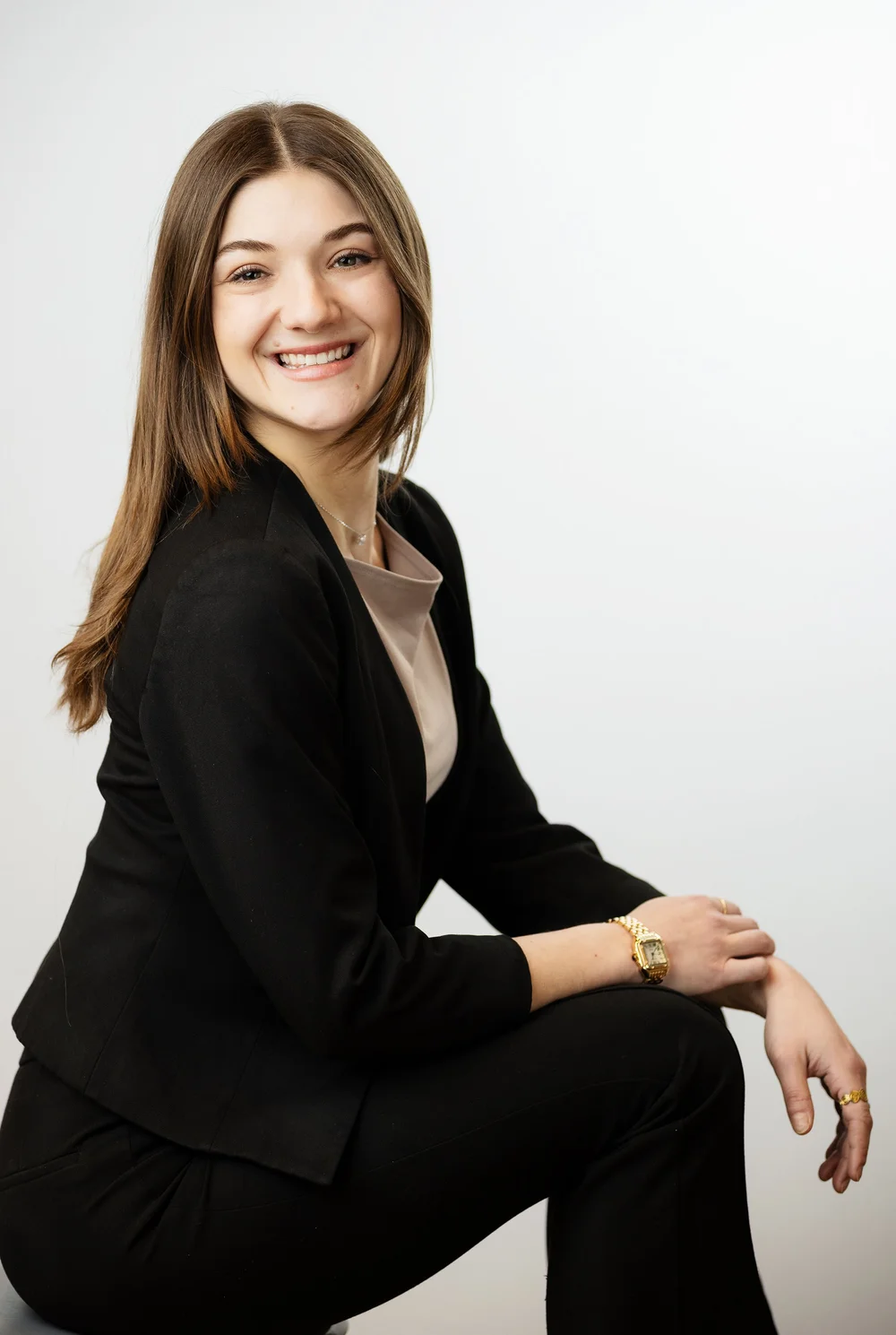 Relaxed seated headshot of a young professional in a black suit on a white background