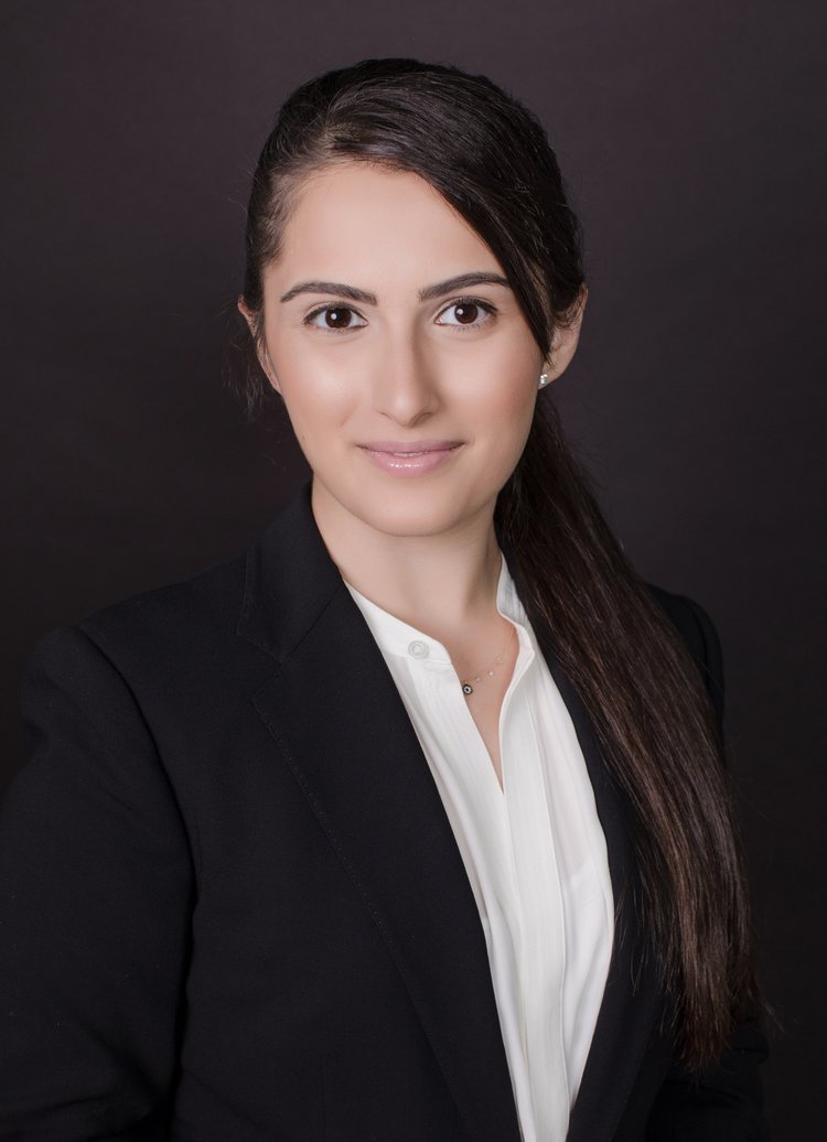 Studio headshot of a physician with long dark hair in a black blazer on a dark background