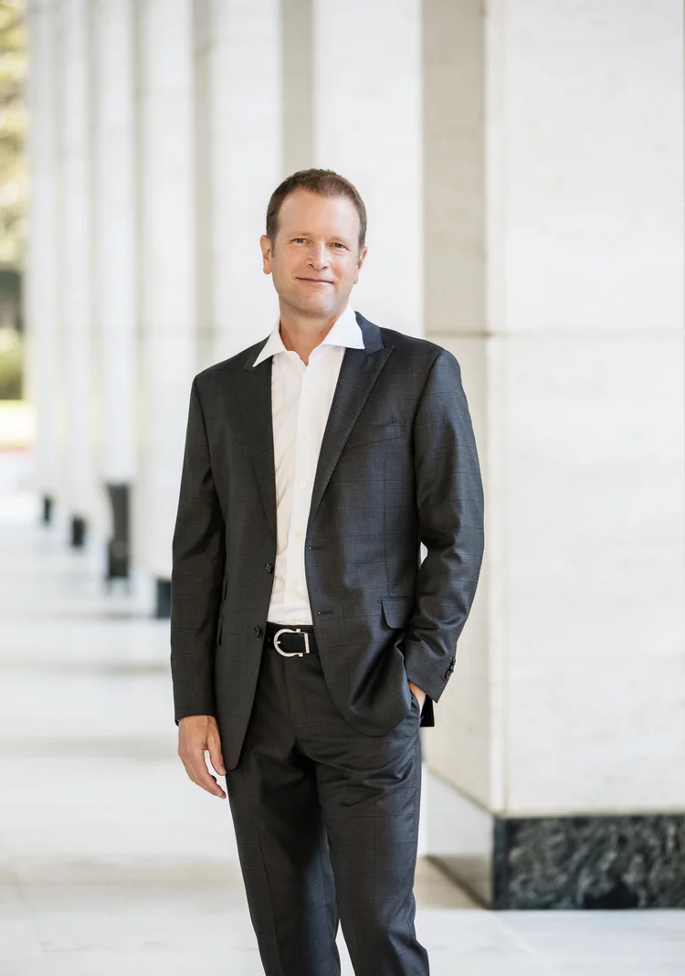 Full-length executive portrait of a man in a dark suit outside an office colonnade