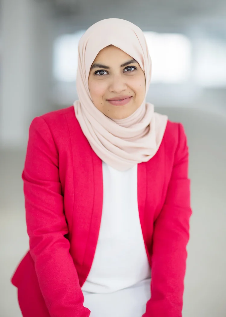 Executive headshot of a woman in a hijab and bright pink blazer in a light-filled office