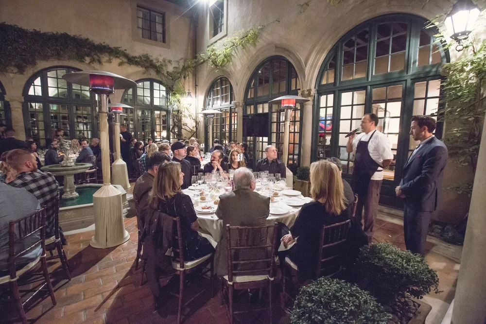 Guests at a corporate dinner listening to a speaker in a warmly lit restaurant