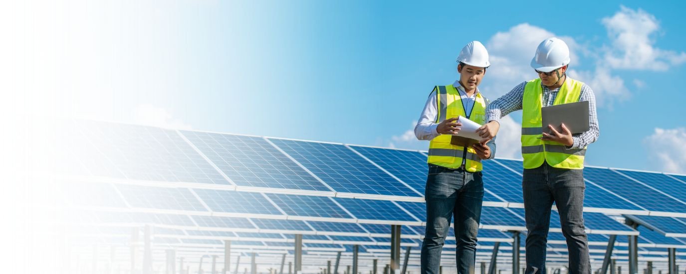 Two engineers wearing safety helmets and vests inspecting solar panels on a sunny day.