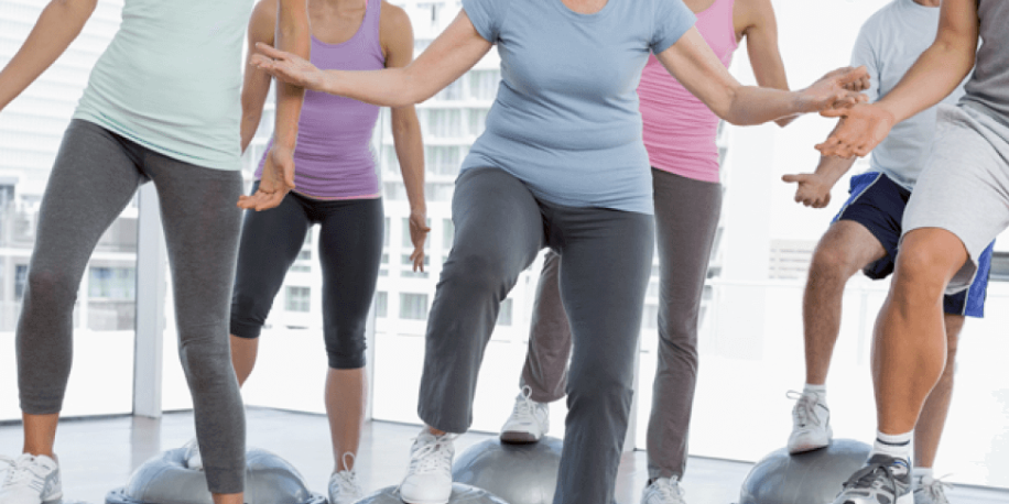 Group fitness class with people stepping on aerobic platforms in a bright, modern gym.