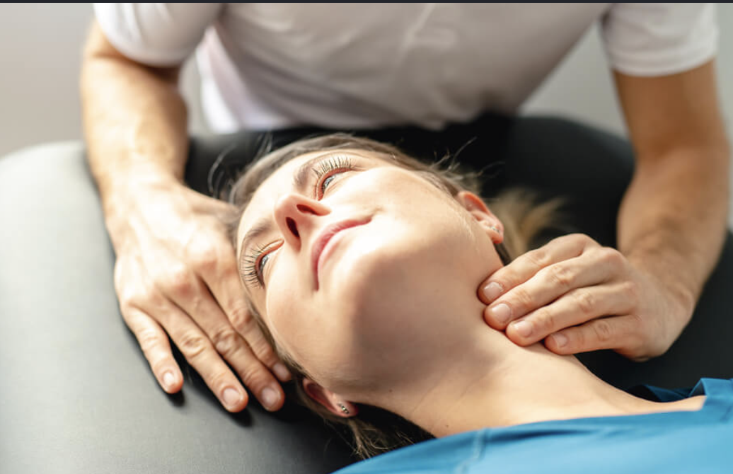 Person receiving a massage or chiropractic adjustment on their neck while lying down with a relaxed expression.