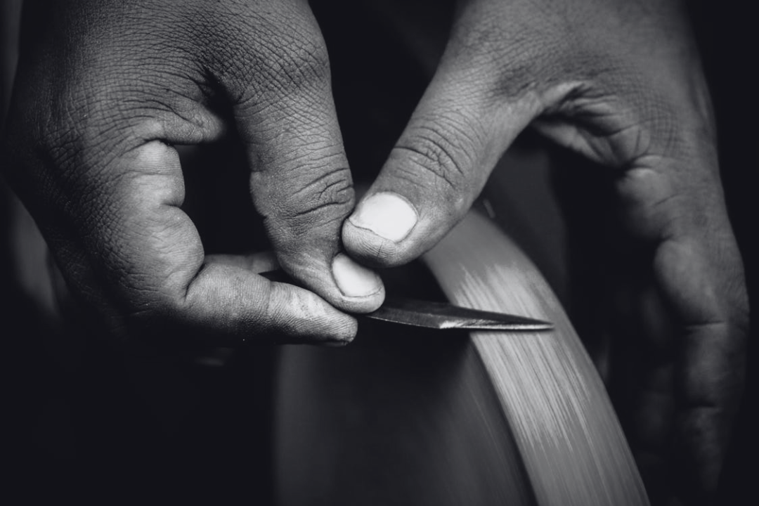 Close-up of a person's hands carving wood with a small chisel.
