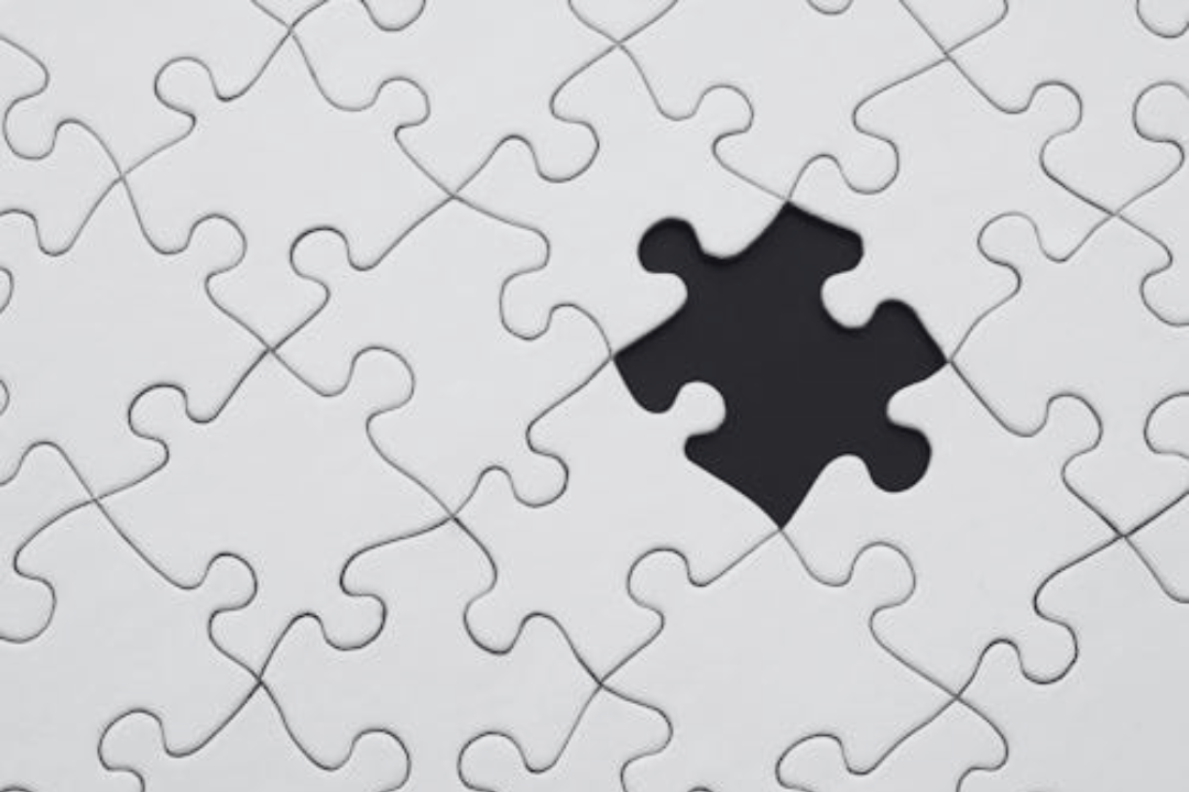 Close-up of a partially assembled white jigsaw puzzle with one black puzzle piece fitting into an empty spot.