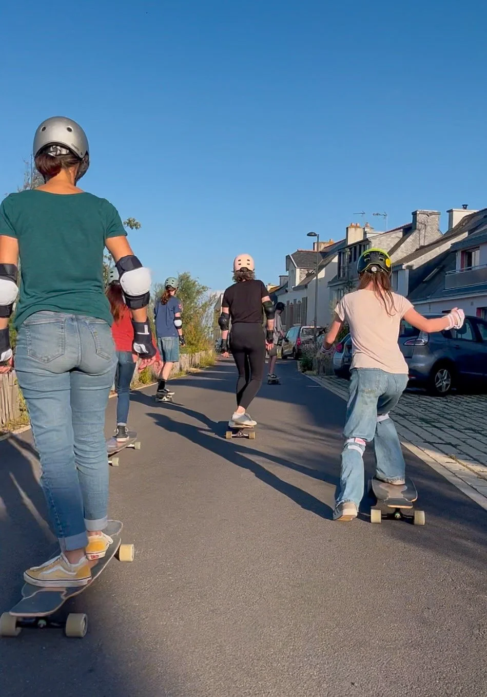 Groupe de personnes faisant du skateboard dans une rue résidentielle sous un ciel clair.