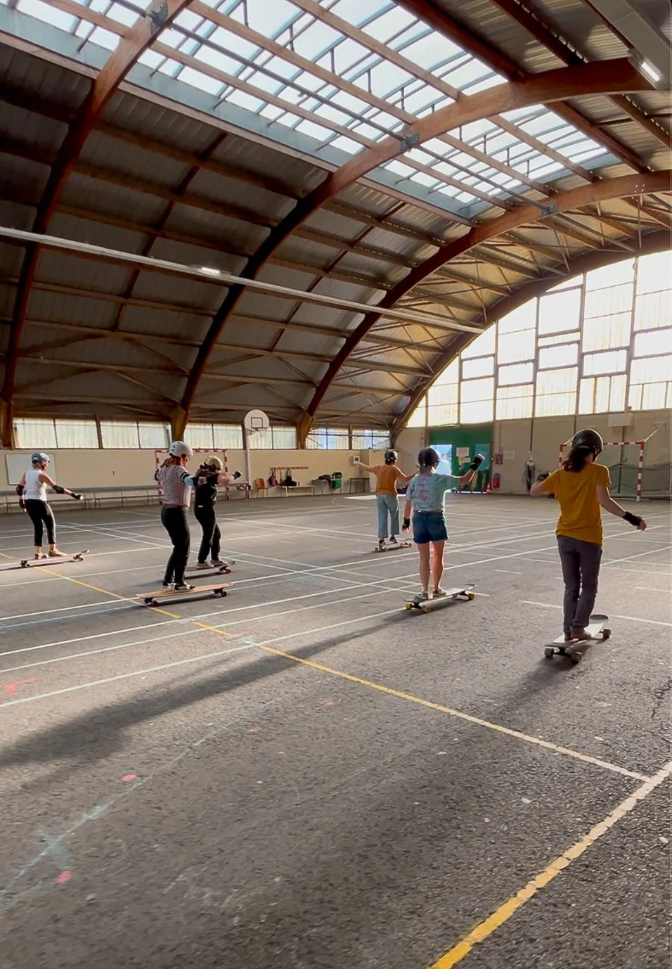 Des enfants faisant du skateboard dans un gymnase avec un plafond en arc en bois et en verre.