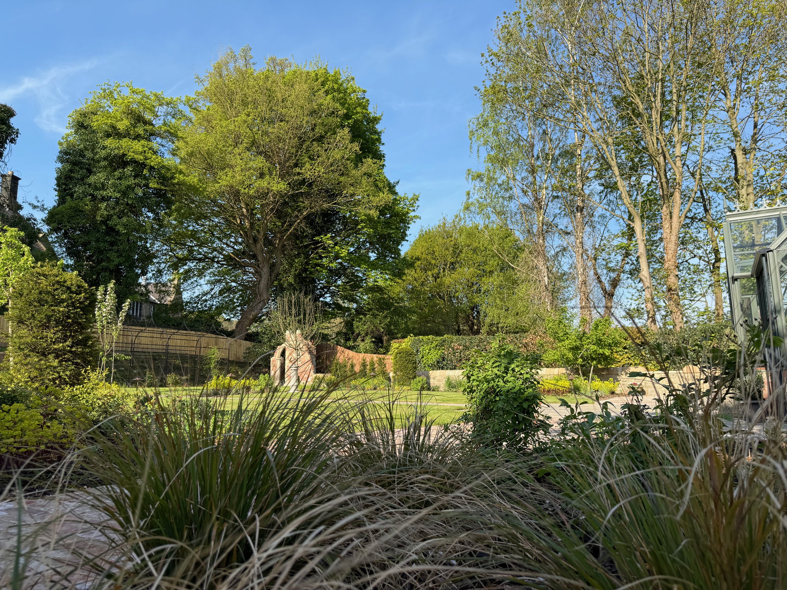 A newly planted garden with a folly and greenhouse