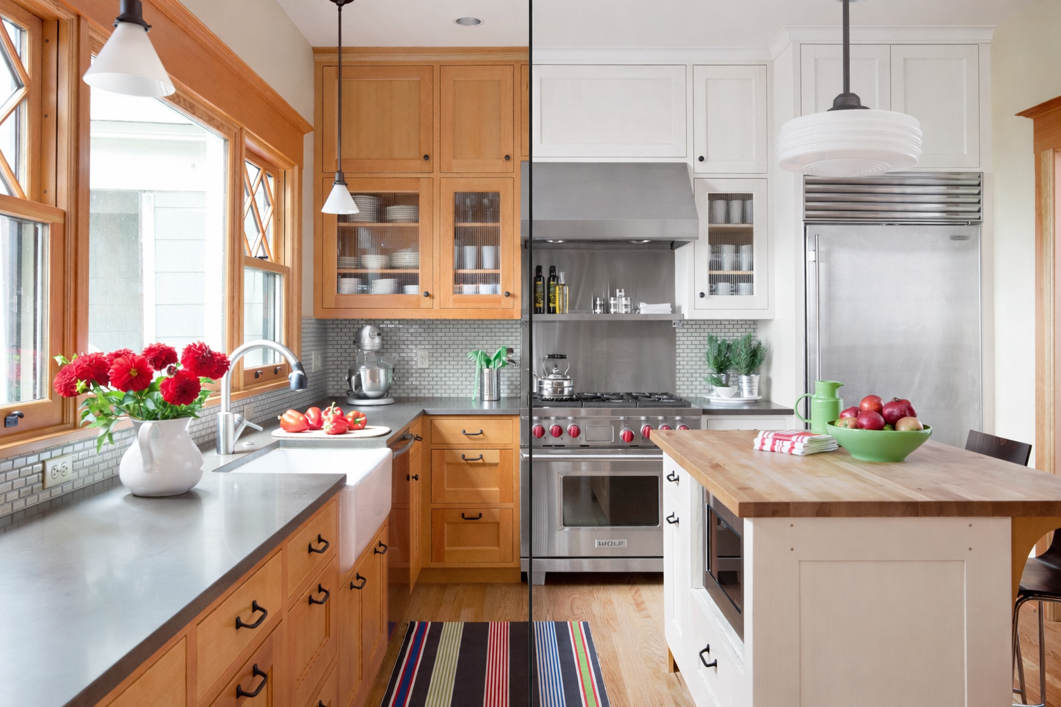 A kitchen split into two contrasting styles: left side with natural wood cabinets, red flowers, and a farmhouse sink; right side with white cabinets, stainless steel appliances, and a wooden kitchen island with apples and a green pitcher.