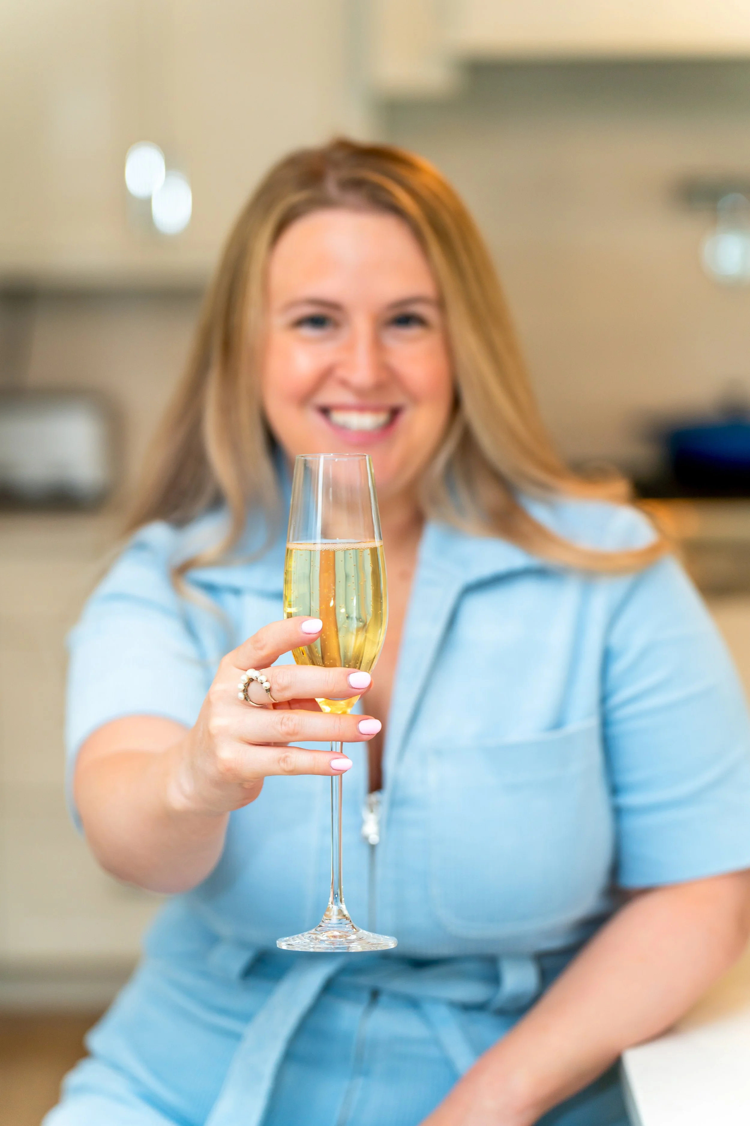 A woman with long blonde hair wearing a light blue shirt holding a glass of champagne