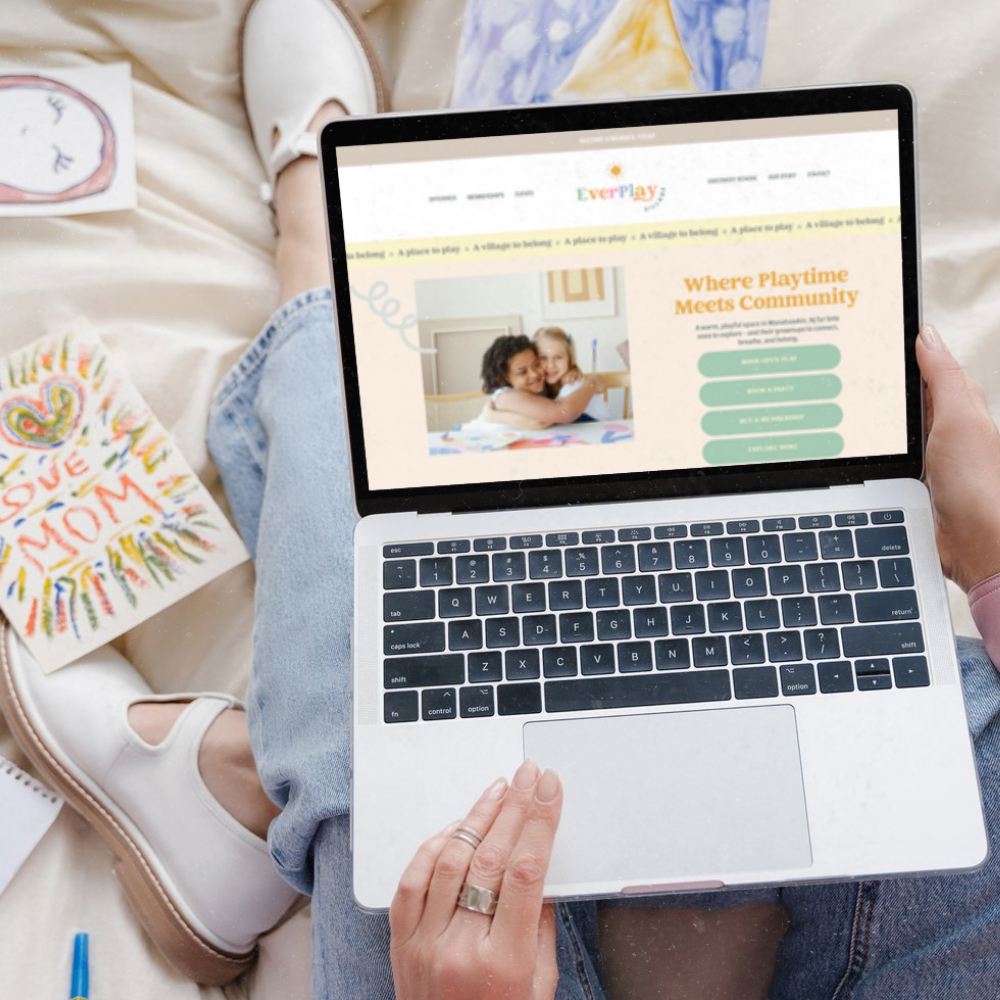 Person holding a laptop while sitting on a bed, browsing a website called EverPlay, which offers community play activities for children.