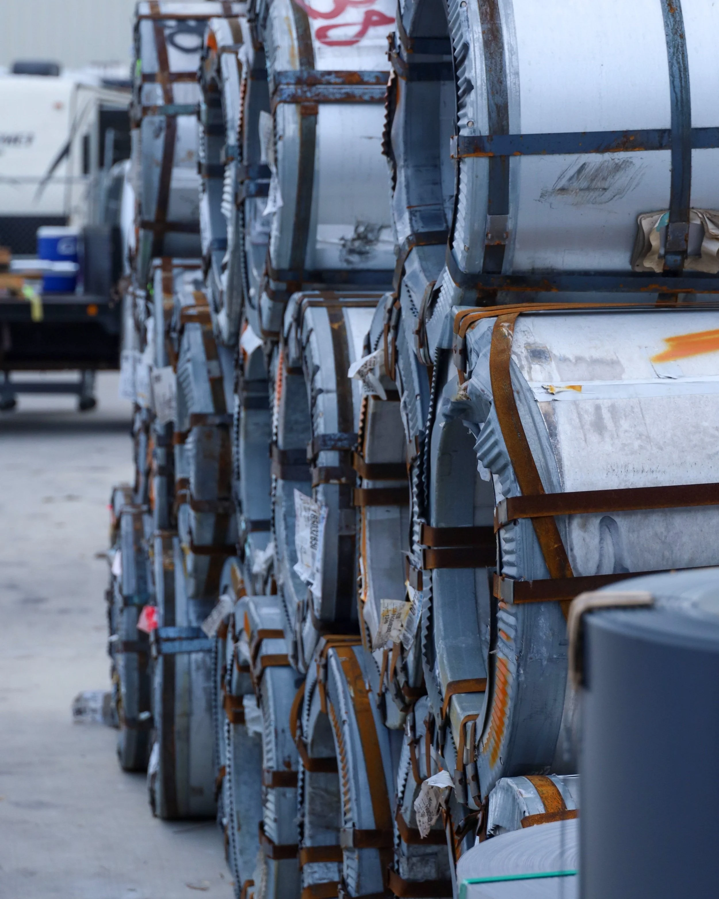 Stacks of metal coils in a storage facility, showcasing materials used for sustainable metal roofing, emphasizing recyclability and durability.