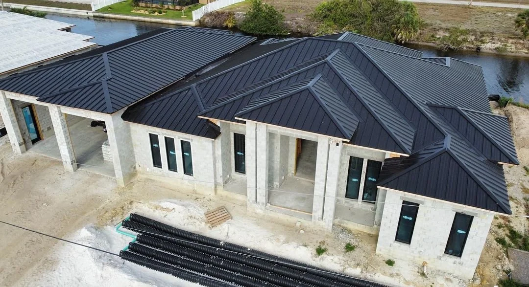 Aerial view of a modern home under construction featuring a sleek black metal roof, surrounded by a natural landscape and a waterway, highlighting durable roofing solutions relevant to Metal Maniacs in Fort Myers.