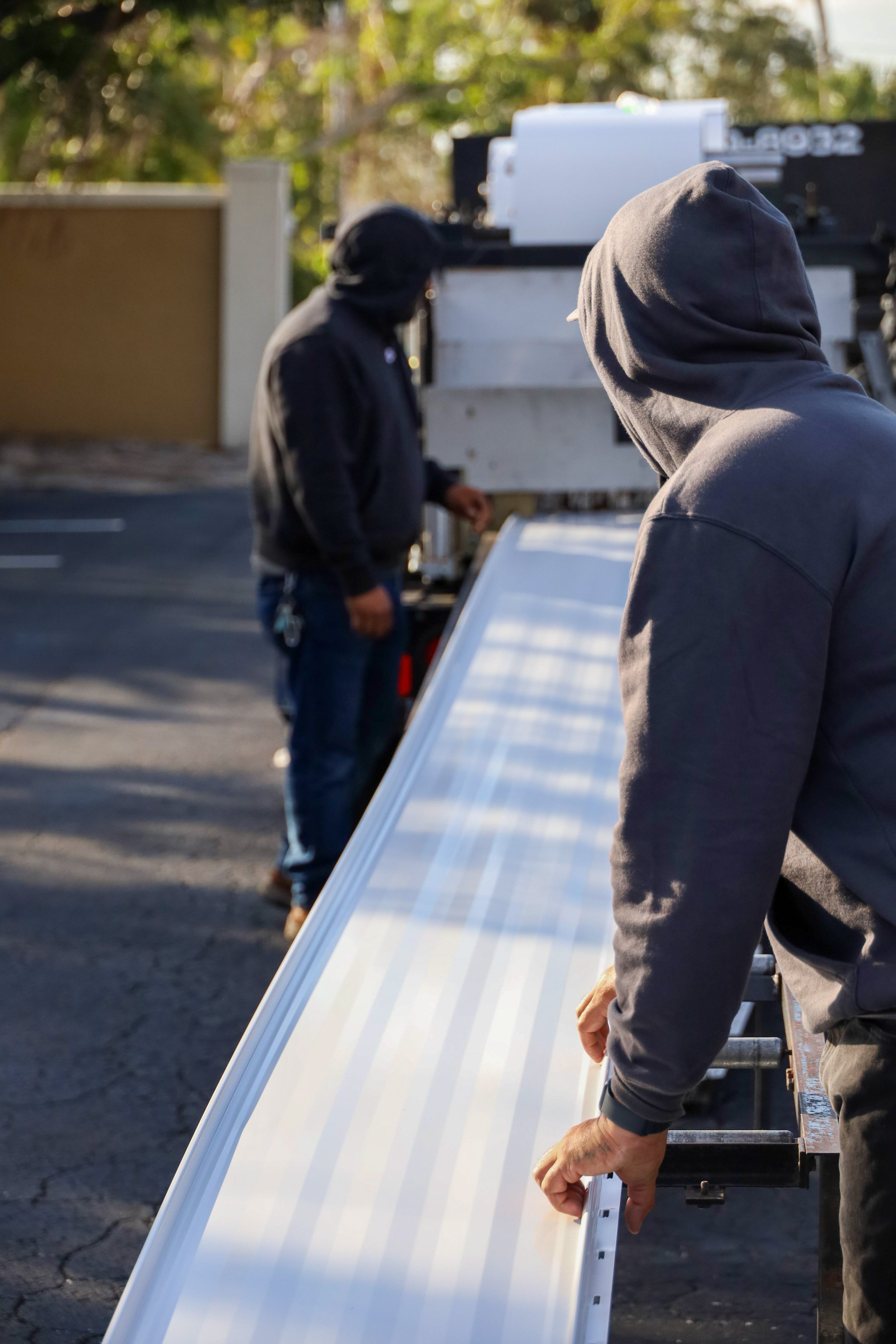 Two workers in hooded sweatshirts handling metal roofing sheets, demonstrating the installation process, with a truck in the background, highlighting innovations in the metal roofing industry.