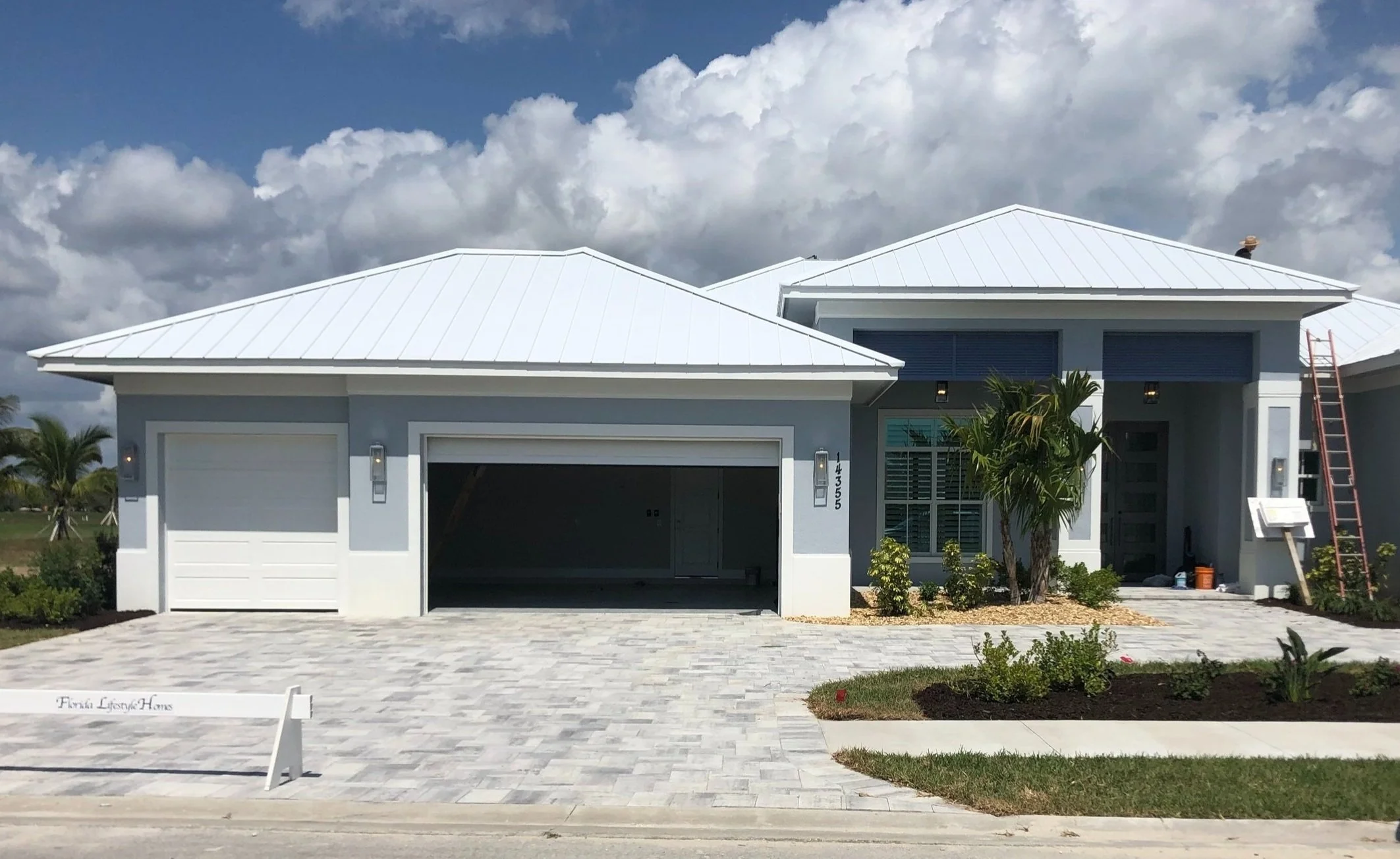 Modern home with standing seam metal roof, featuring a two-car garage, landscaped front yard, and decorative exterior lighting.