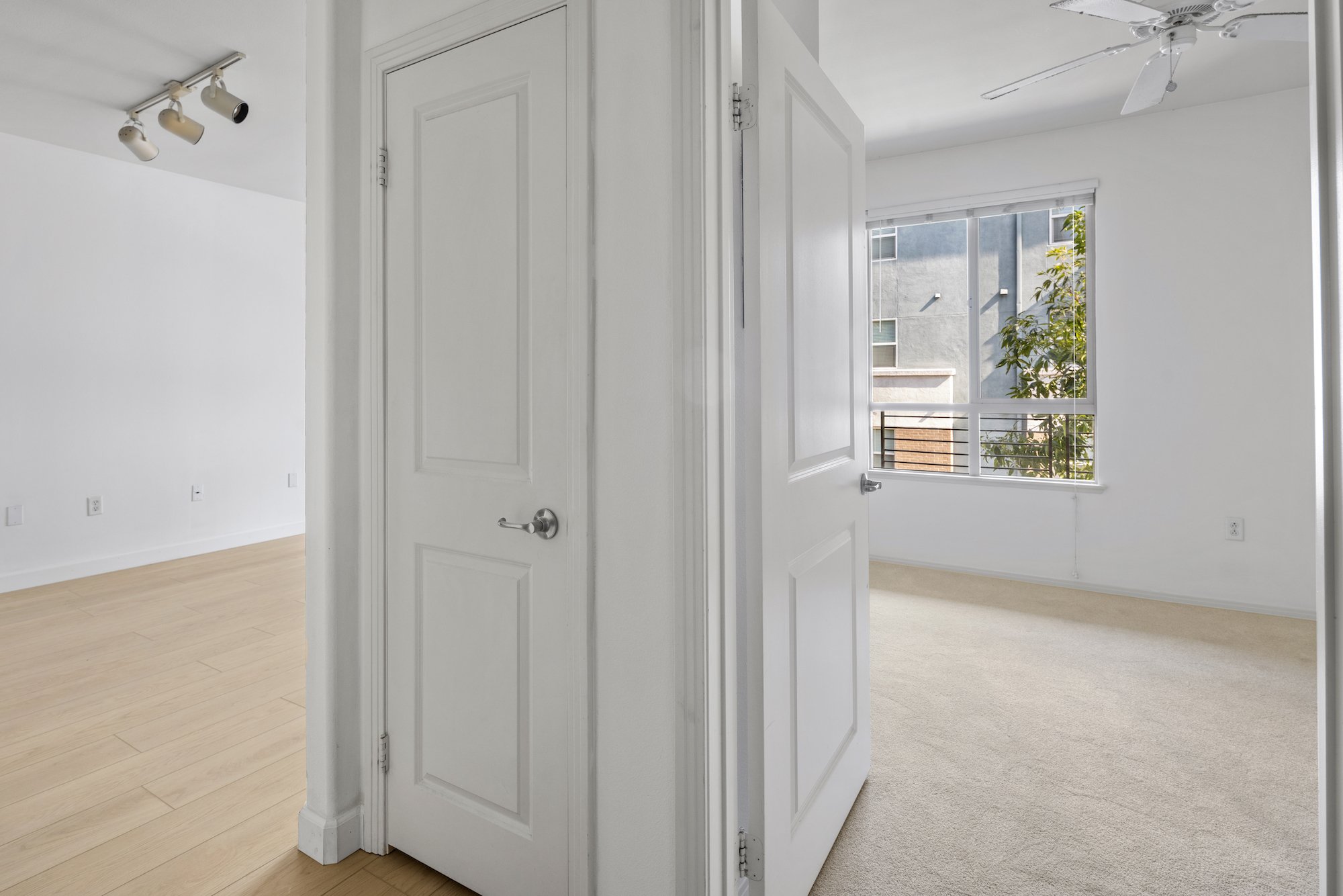 An Downtown Los Angeles condo with white walls, a window, beige carpet, and a ceiling fan.