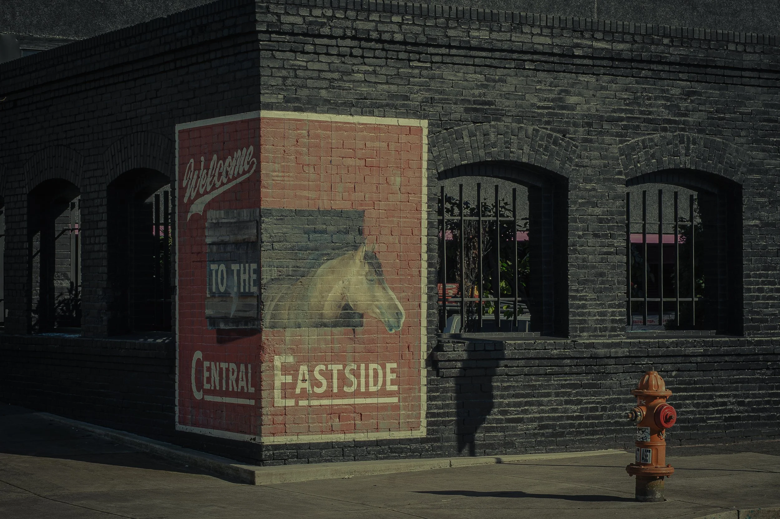 A painted mural on a brick corner building depicting a horse's head and the words 'To the Central Eastside' on a red background.