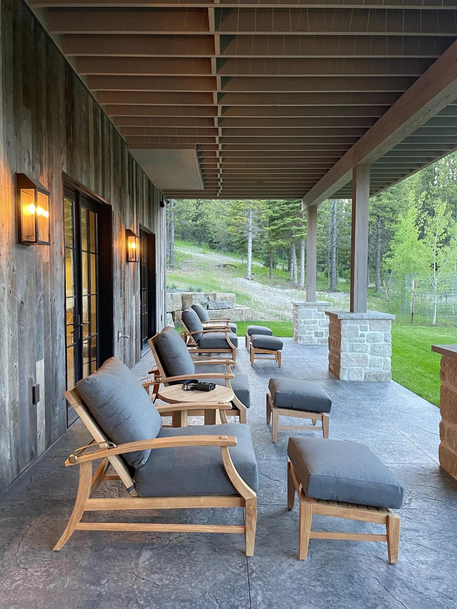 Rustic modern luxury new construction ski home in Big Sky Montana designed by Hive Home. Patio with teak organic modern furniture with earthy texture. A cozy spot to take in the unbelievable Spanish Peaks mountain views