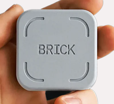 A gray square object with the word "BRICK" embossed in the center, being held between human fingers.
