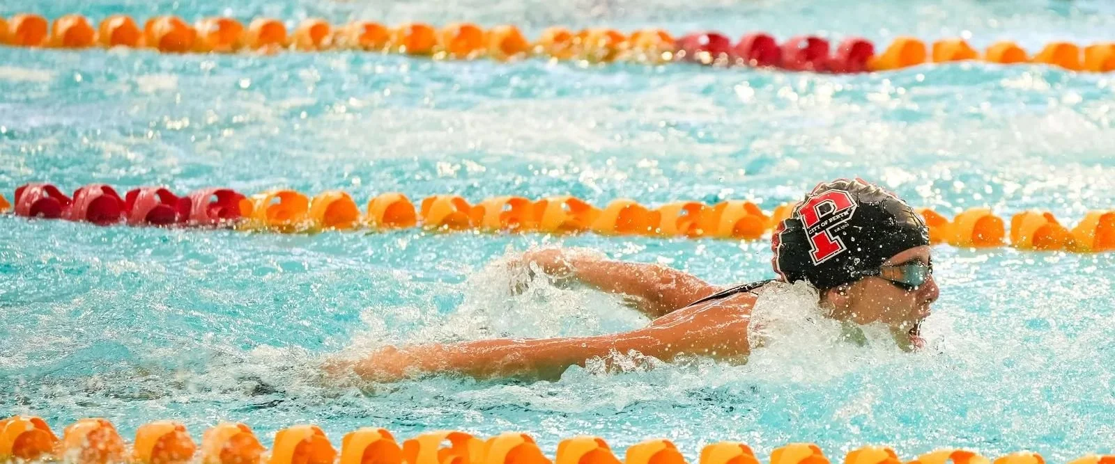 Swimmer wearing a cap with the number 1 and goggles, swimming freestyle in a pool with orange and yellow lane dividers.