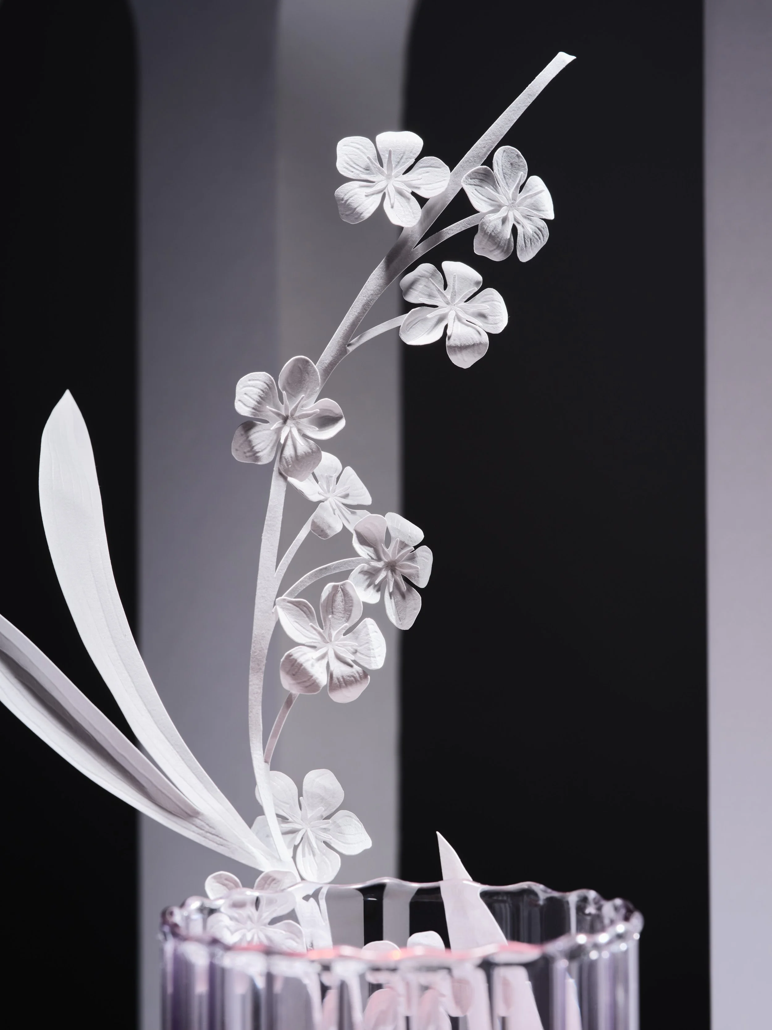 intricate white paper flowers on a vine in a pink glass vase