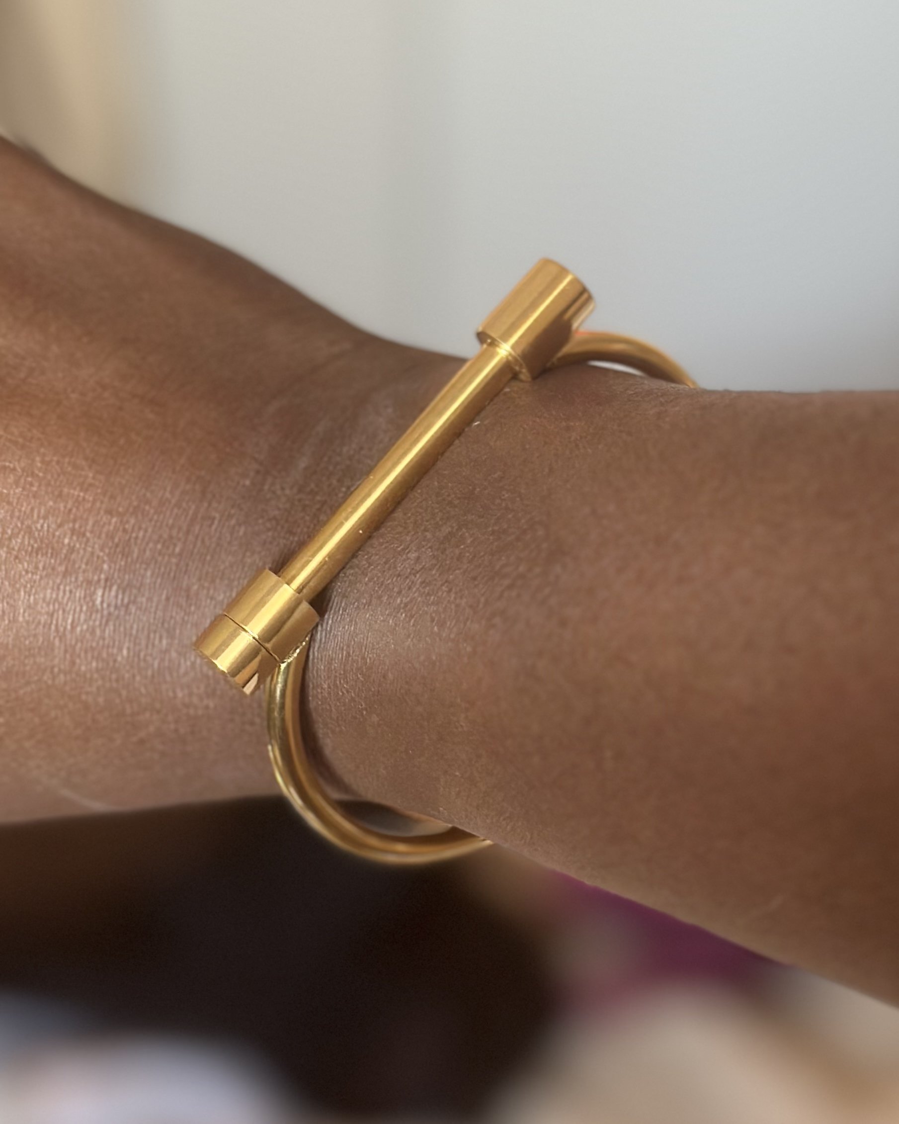 Gold Athena bangle resting on textured linen, showcasing minimalist T-bar clasp and circular shape