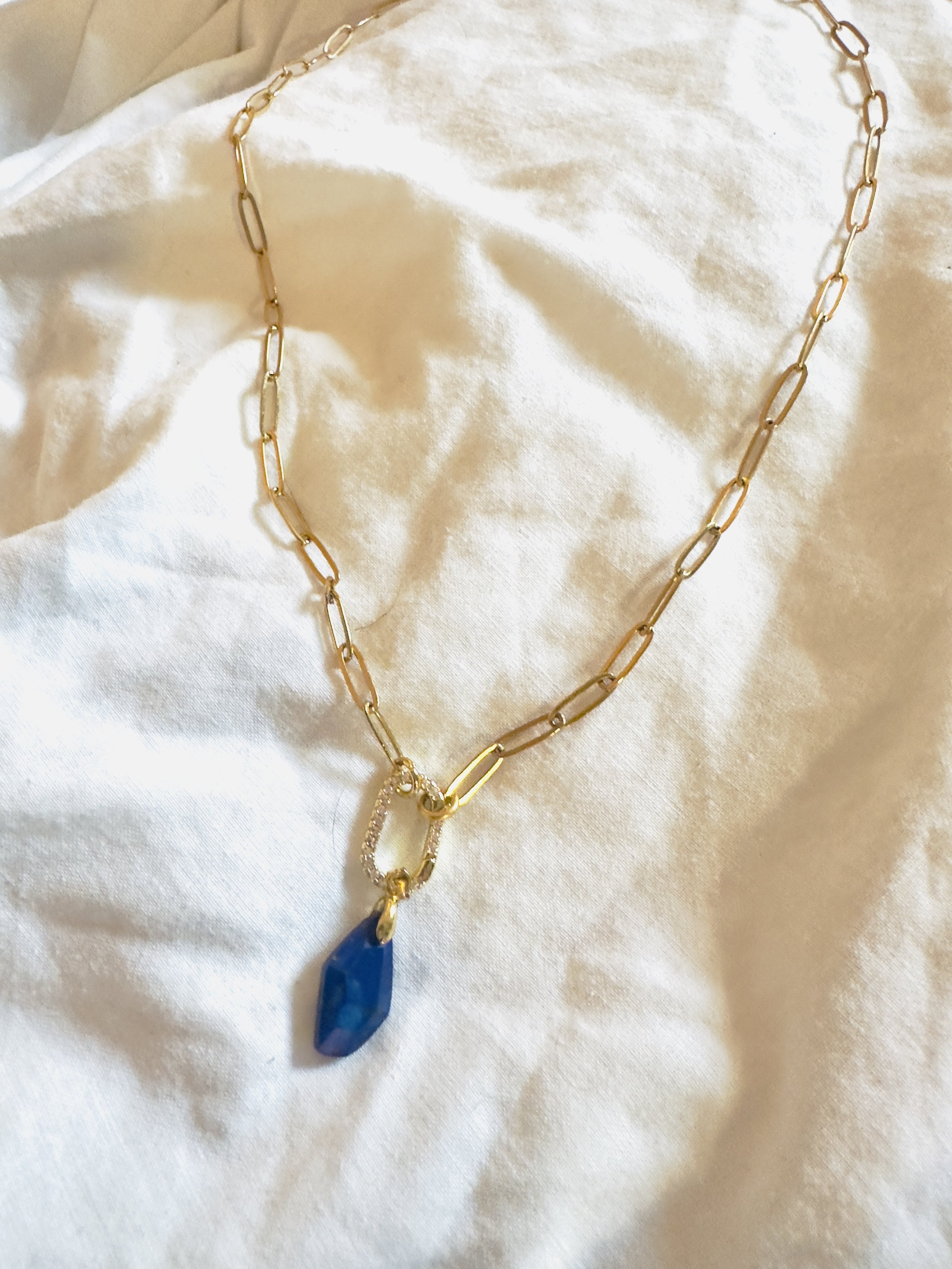 Full view of the Caelia Necklace with gold paperclip chain and lapis lazuli pendant, styled flat on soft fabric.