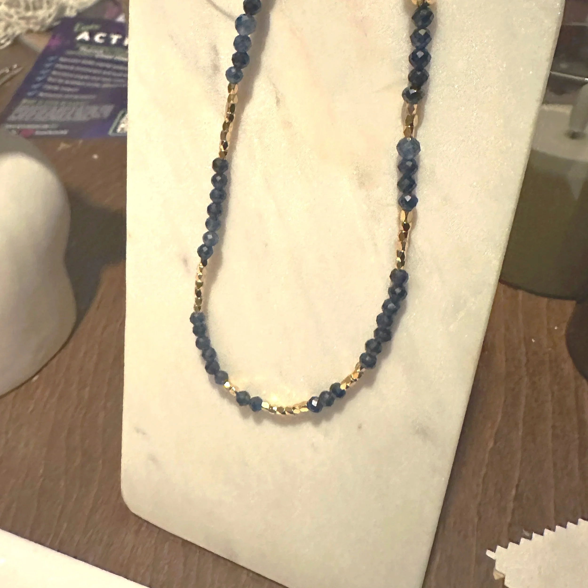 Sapphire gemstone necklace on gold chain with gold bead detailing.