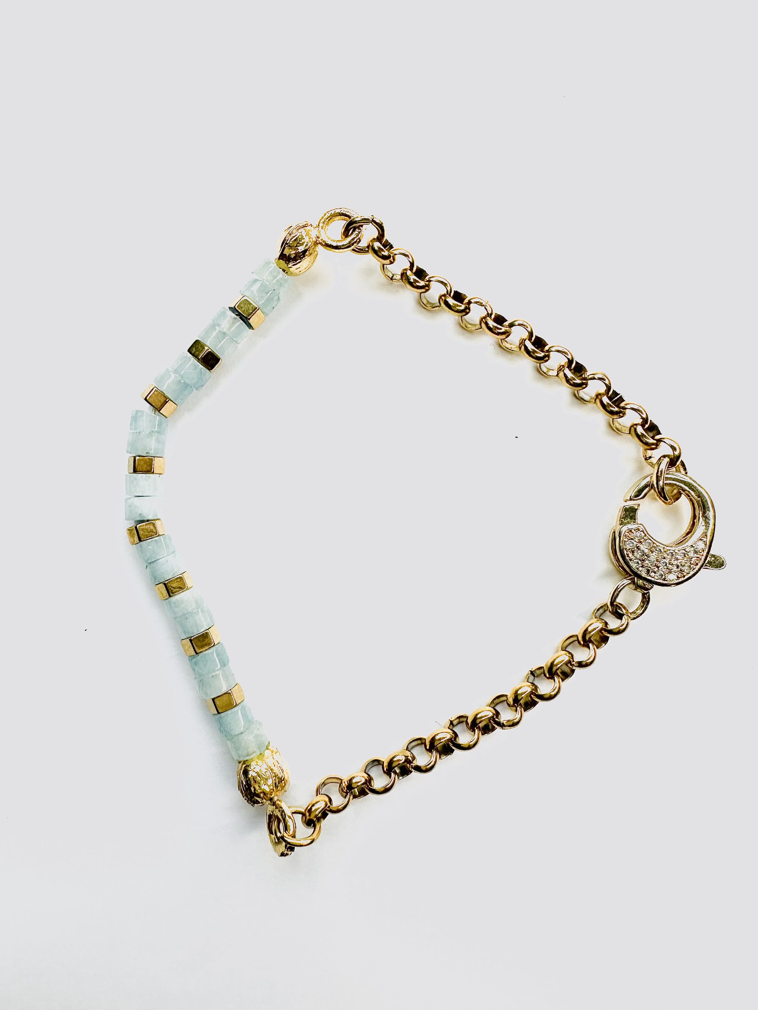 Aquamarine Ibeji Bracelet displayed on natural linen, showcasing its elegant gold chain and vibrant gemstone beads.