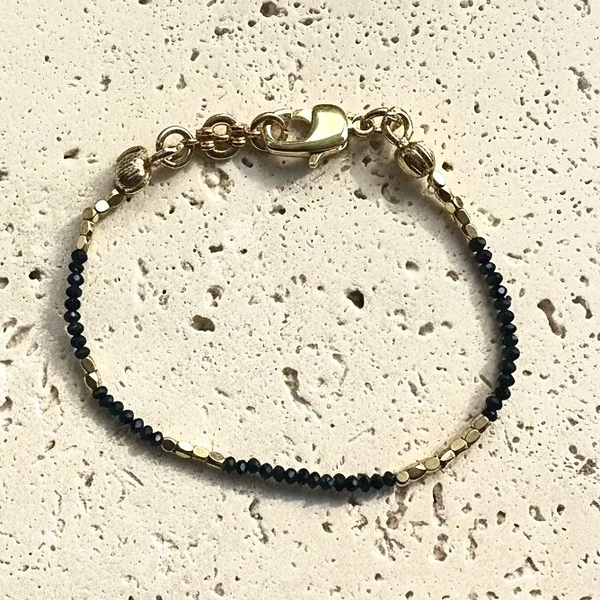 Black spinel beaded bracelet with gold tone accents on neutral background
