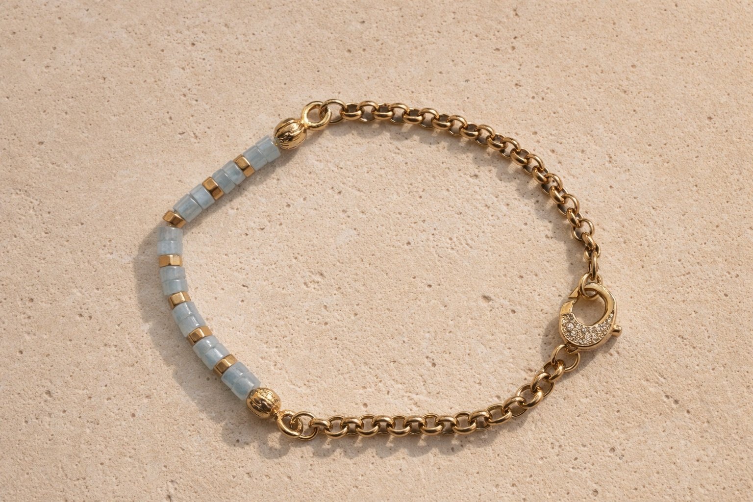 Aquamarine beaded bracelet with gold detailing on pale stone surface