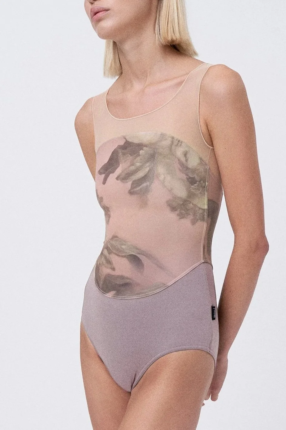 A woman wearing a beige sleeveless bodysuit with a printed face and floral design, paired with matching high-waisted underwear, standing against a plain white background.