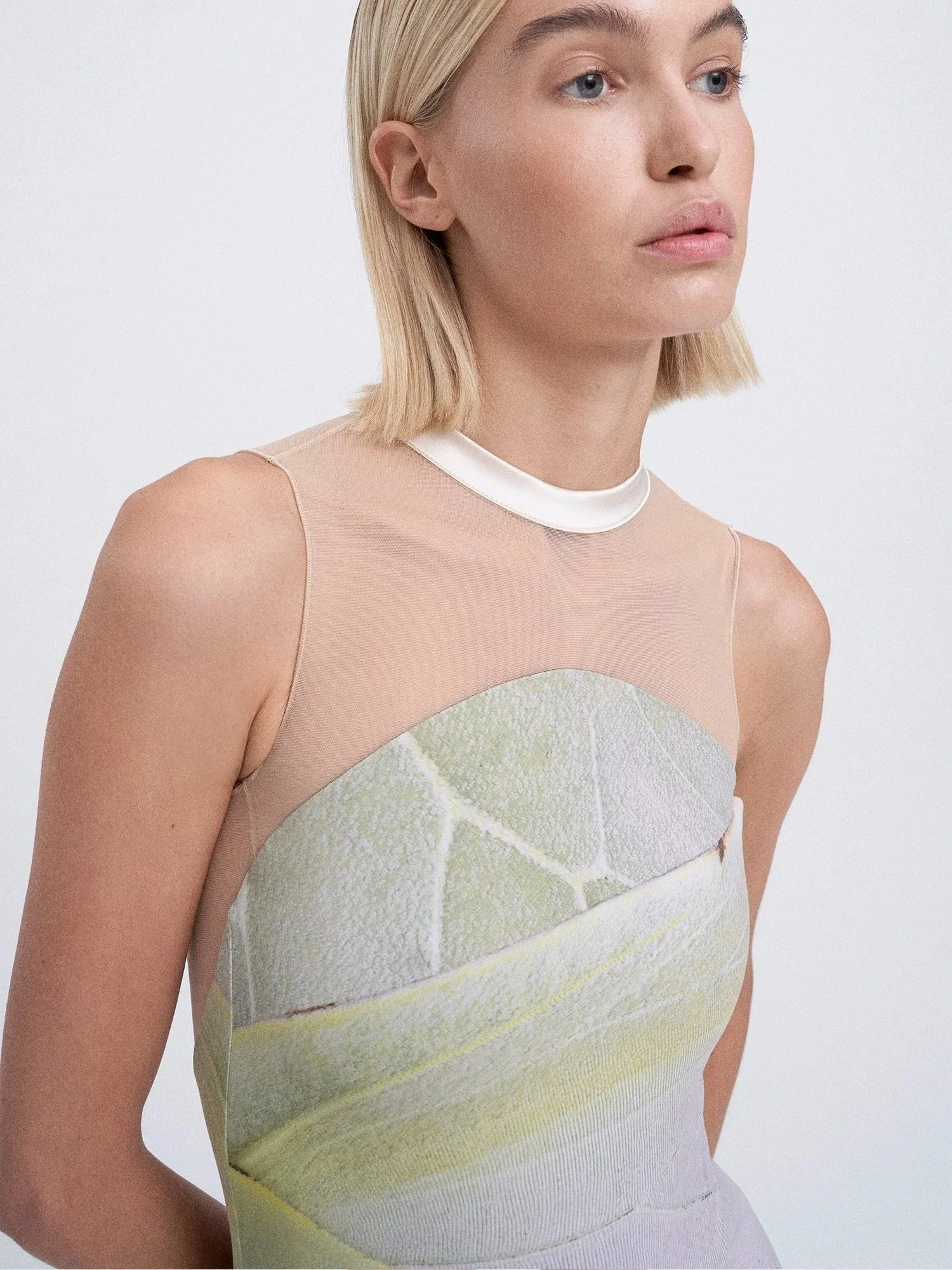 A woman with blonde hair wearing a sleeveless dress with a leaf print design.