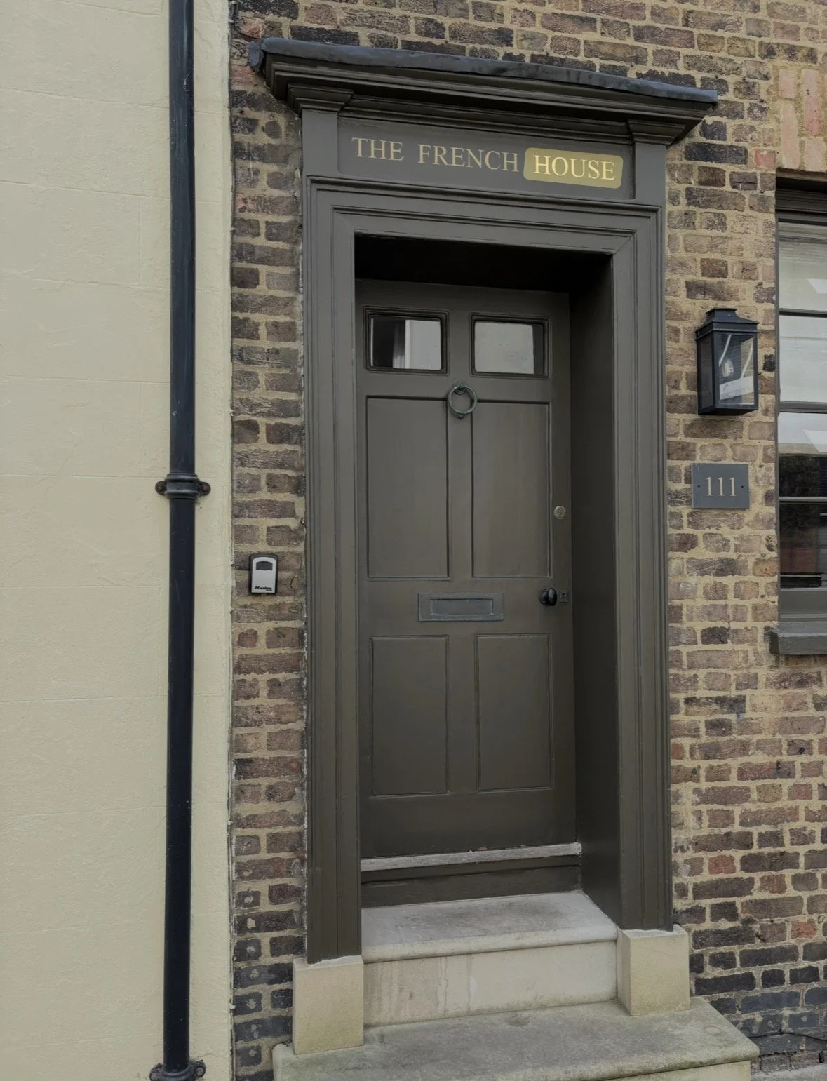 Front entrance of a building with a dark gray door, brick walls, and a sign reading 'The French House' above the door.