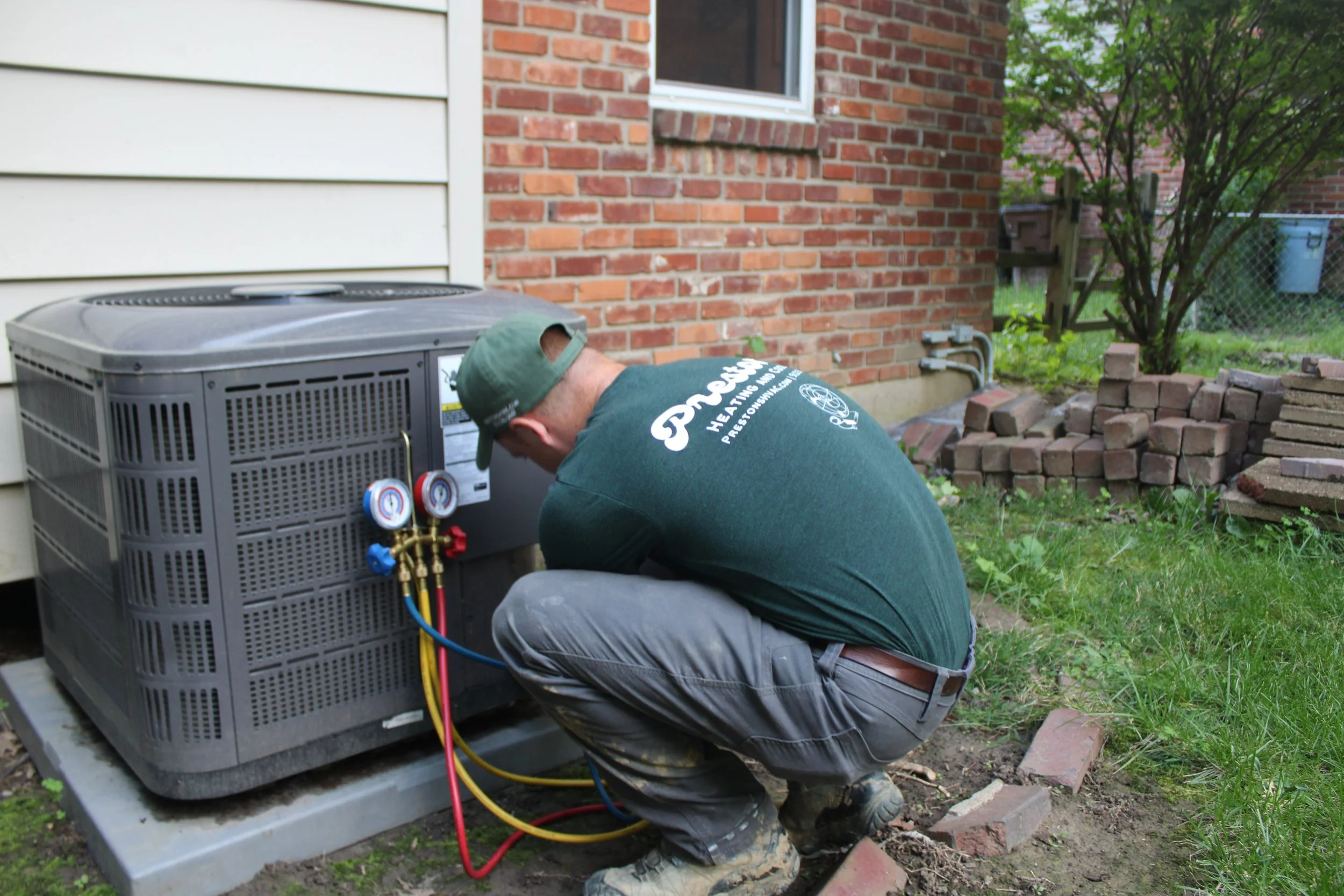 Man in green shirt and hat works on an AC unit outside in Cincinnati Ohio