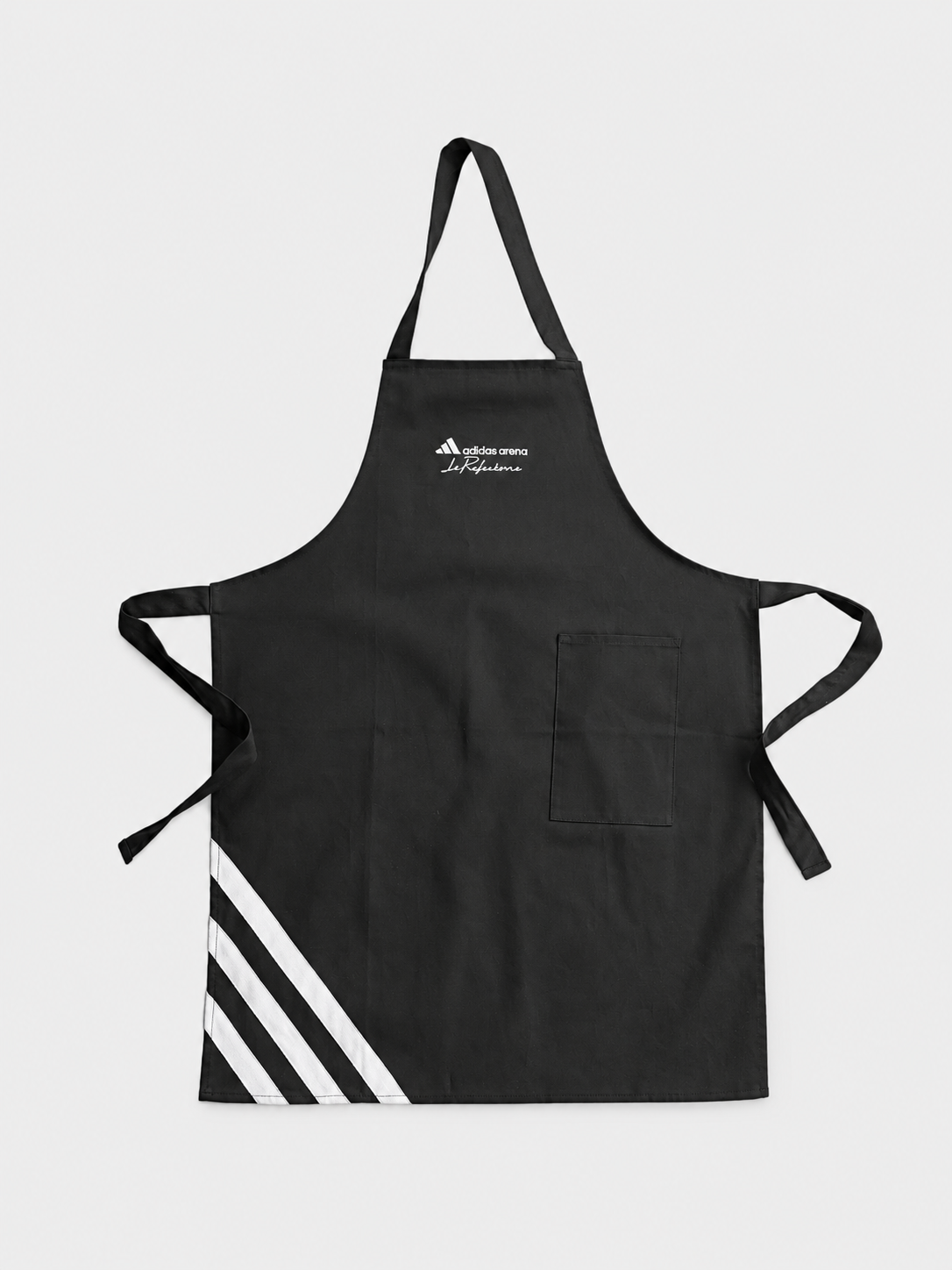 Tablier noir avec logo Adidas, marqué adidas arena et le Fouleur. Faite en tissu, avec une poche sur le côté droit, trois bandes blanches en bas à gauche, liens pour attacher autour de la taille, et une cordelière pour le cou.