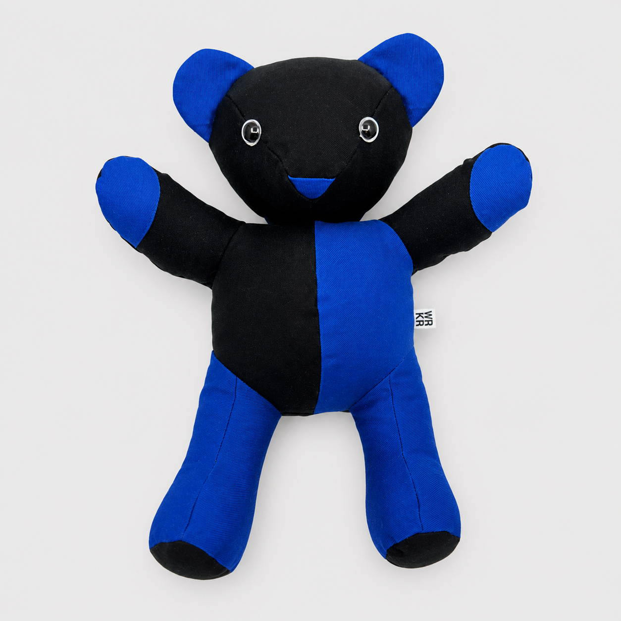 Un doudou en forme d'ours, de couleur noire et bleue, avec des yeux en boutons et un sourire en tissu noir.