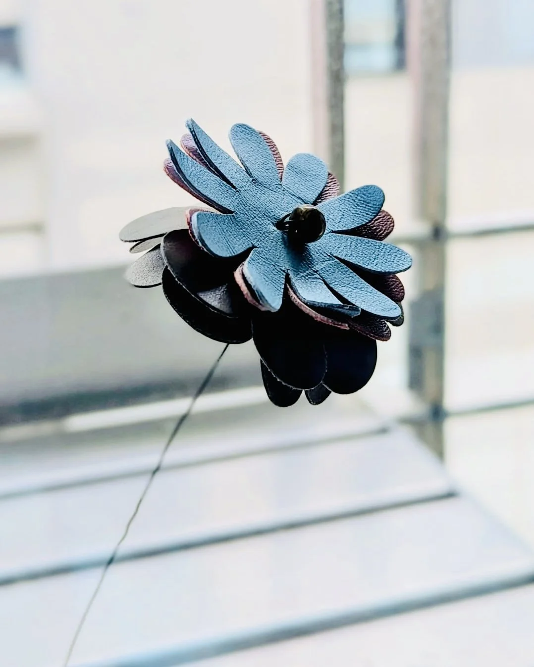 Une fleur artificielle en bois ou en tissu, principalement bleue, avec un bouton noir au centre, fixée à un fil ou une tige fine.