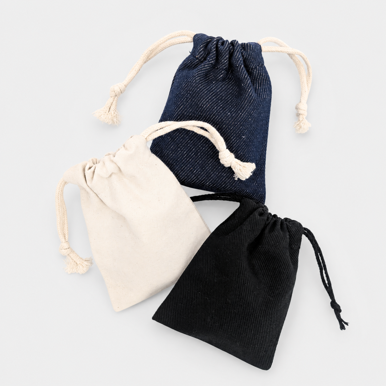 Trois petits sacs en tissu de différentes couleurs (bleu, beige et noir) avec des cordons à pompons.
