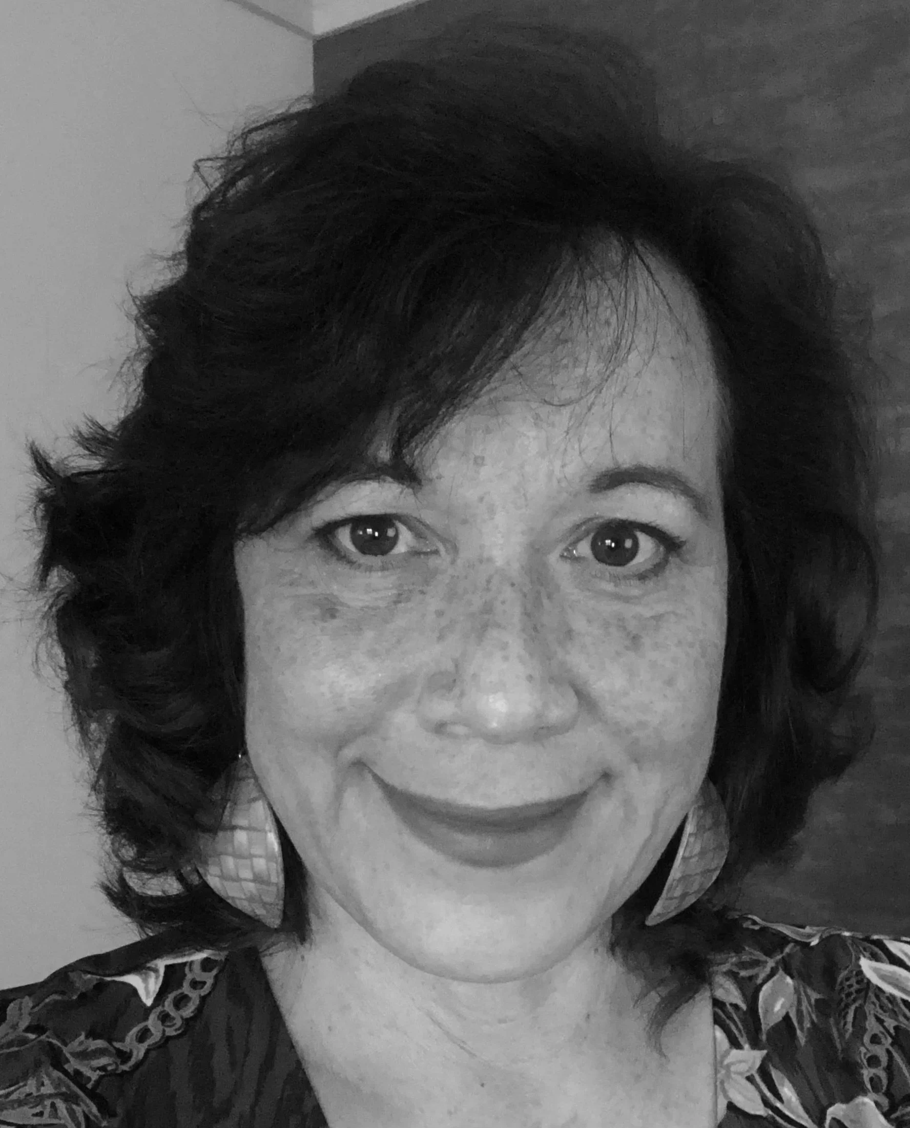 A woman with dark, wavy hair and a patterned blouse smiling at the camera.