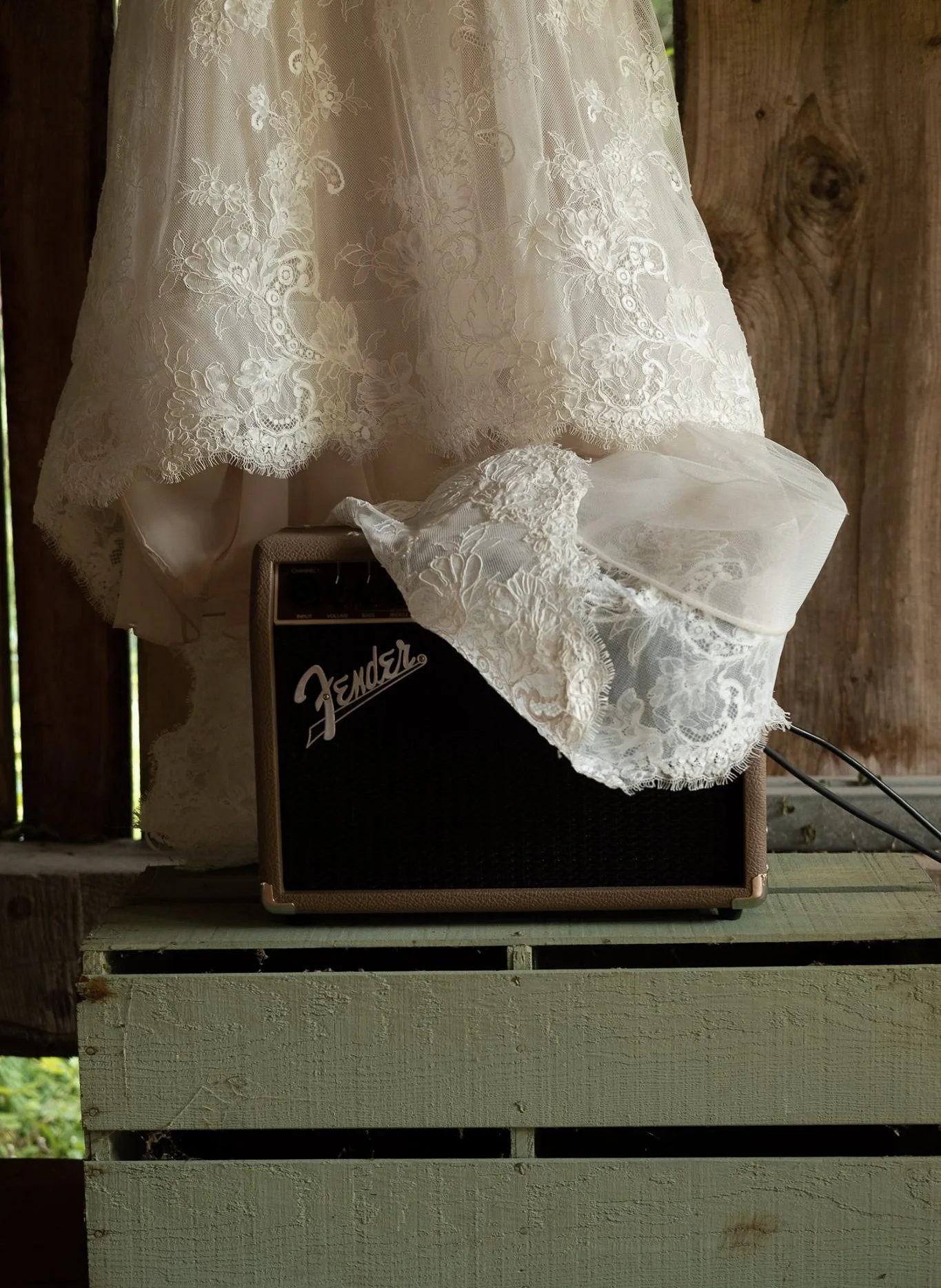 A lace dress draped over a small amplifier on a wooden porch or deck with a wooden wall in the background.