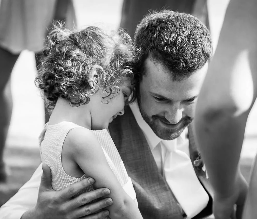 A young girl and a man are sharing a tender moment, with the girl leaning her head on the man's shoulder and the man smiling warmly. The image is in black and white.
